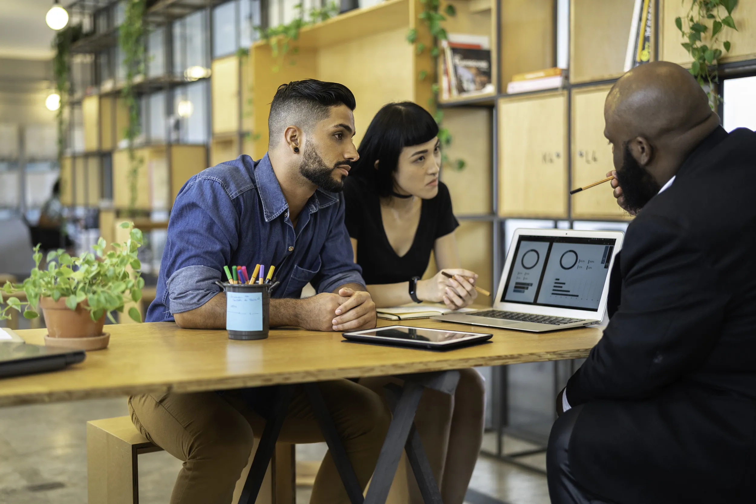 A group of three people gathered around a table, focused on a laptop, discussing ideas and sharing insights.