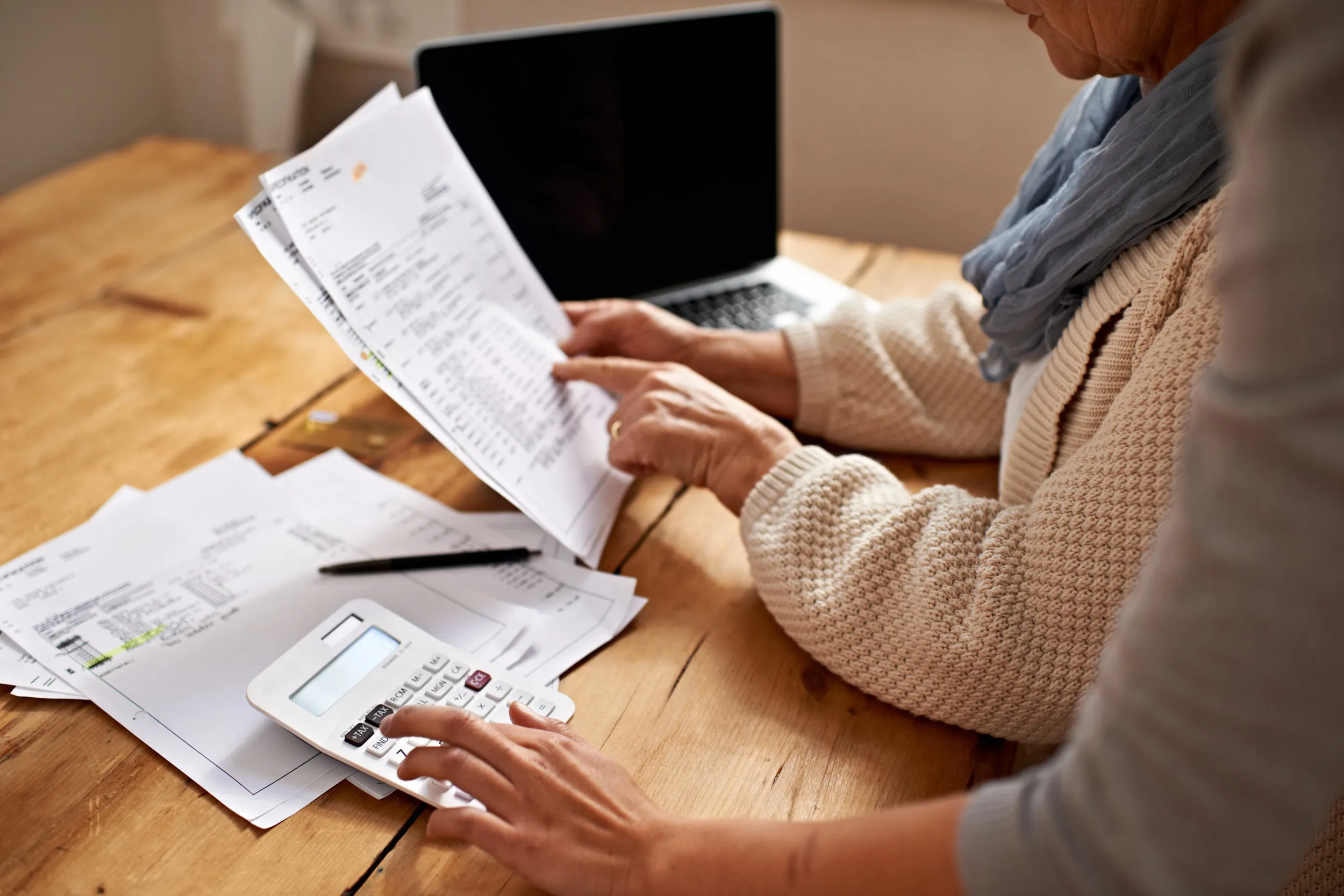 Two people reviewing a document and performing calculations in front of a laptop.