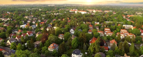 Aerial view of a suburban neighborhood with green trees, houses with red and gray roofs.