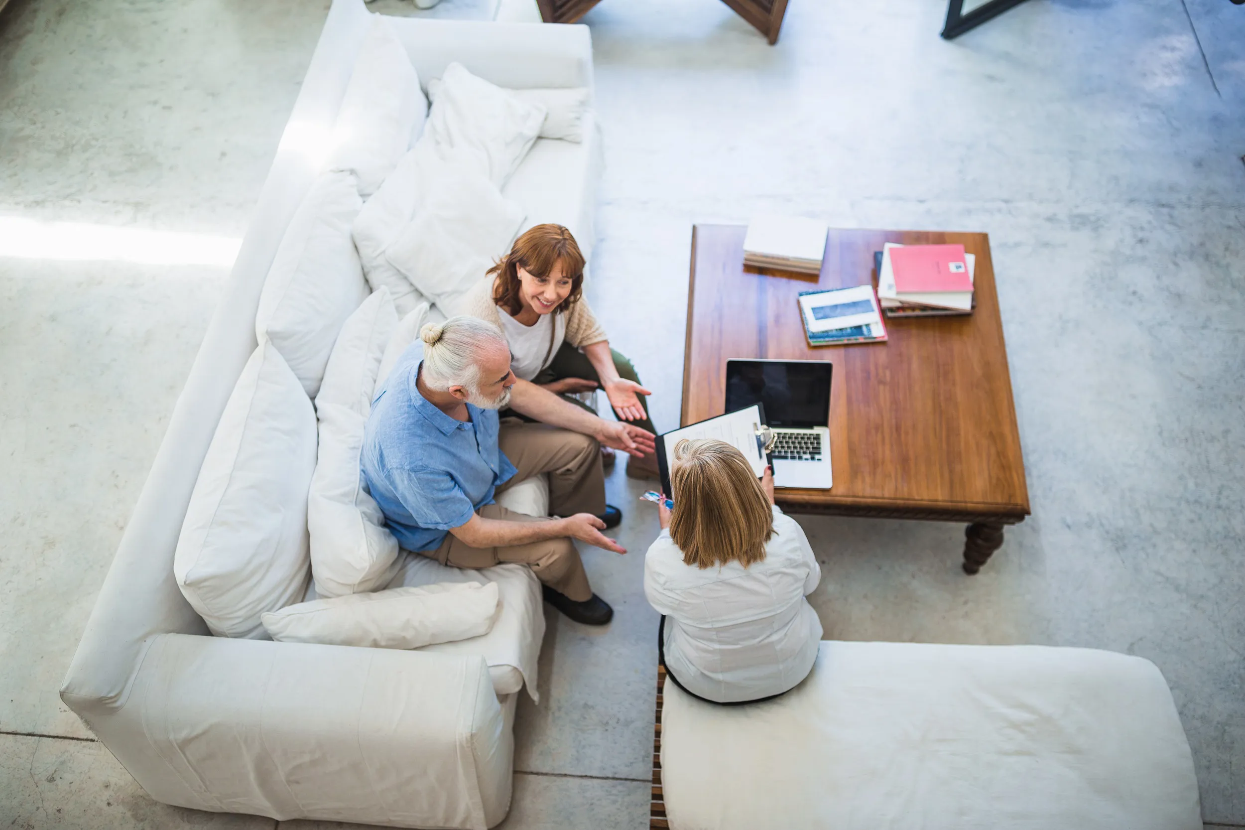 Three individuals seated on a couch, viewing documents while engaged in a conversation.